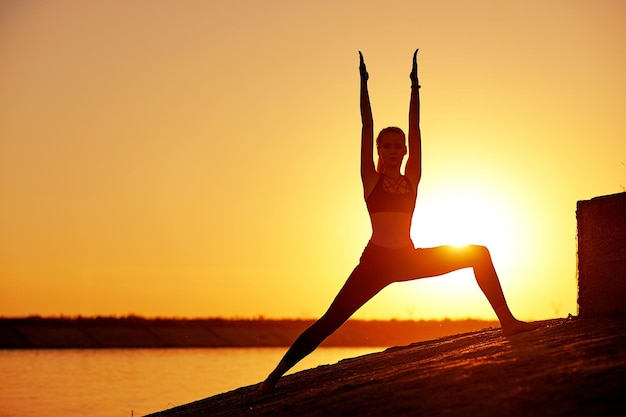 Silueta mujer practicando yoga o estiramientos en el muelle de la playa al atardecer o al amanecer