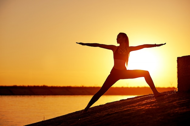 Silueta mujer practicando yoga o estiramientos en el muelle de la playa al atardecer o al amanecer