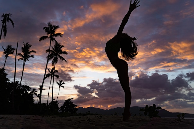 Silueta de mujer durante la puesta de sol tropical con palmeras y nubes dramáticas. Concepto de vacaciones y resort.