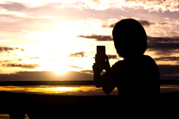 La silueta de la mujer que usa el teléfono elegante toma la foto sobre hermosa