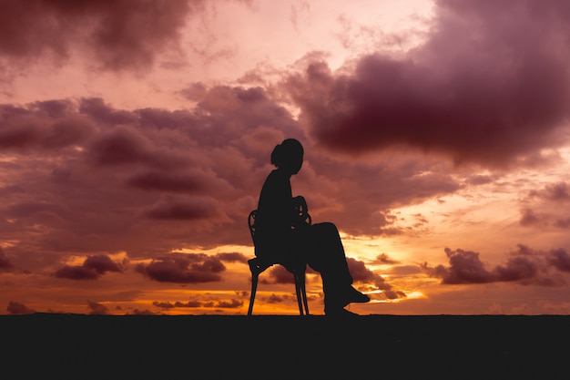 La silueta de una mujer se sienta en una silla con el cielo dramático colorido.
