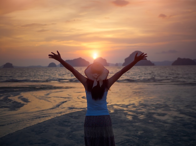 Foto silueta de mujer con sombrero con los brazos abiertos bajo la salida del sol cerca del mar