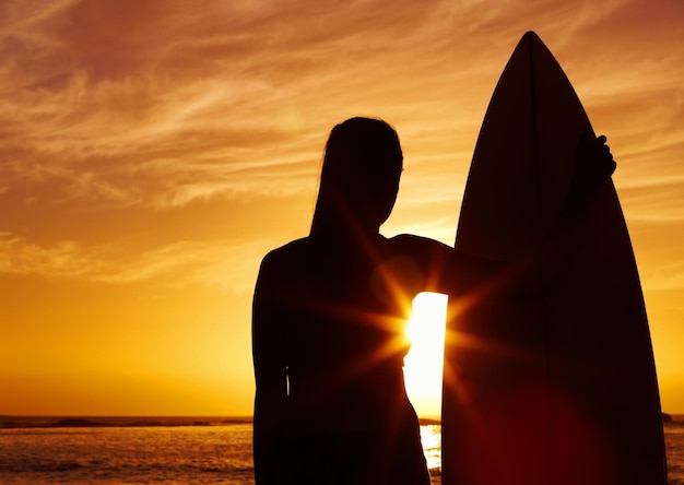 Silueta de una mujer sosteniendo una tabla de surf al atardecer Silueta de una hermosa mujer sosteniendo una tabla de surf al atardecer