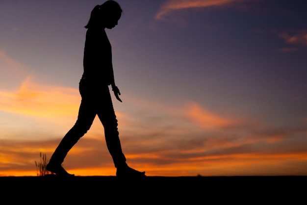 Foto silueta de mujeres tristes y deprimidas caminando en la pasarela del parque con puesta de sol