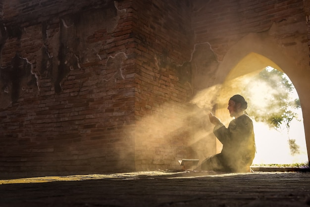 La silueta de un musulmán asiático, que está rezando en una habitación con la luz del sol brillando a través de la puerta de la mezquita