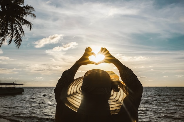 Silueta negra de una mujer en la playa haciendo el amor en forma de símbolo con su dedo recto con el su