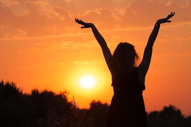 Silueta de una niña al atardecer. Chica y puesta de sol. Silueta de una niña al atardecer con las manos en alto.