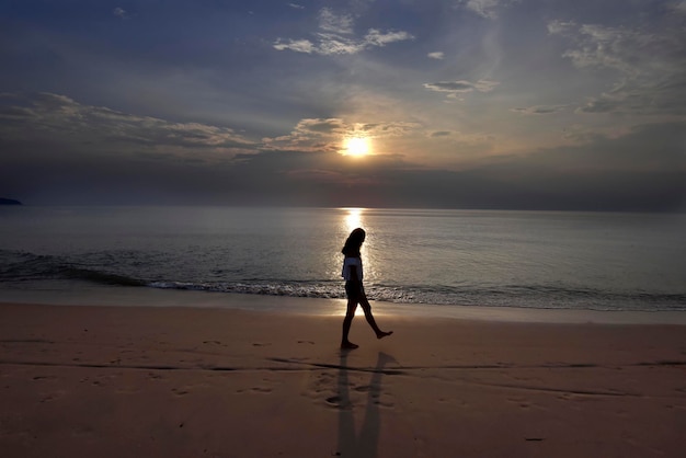 Una silueta de niña caminando en una hermosa playa de Tailandia con una prueba ligera de la superficie del mar al atardecer