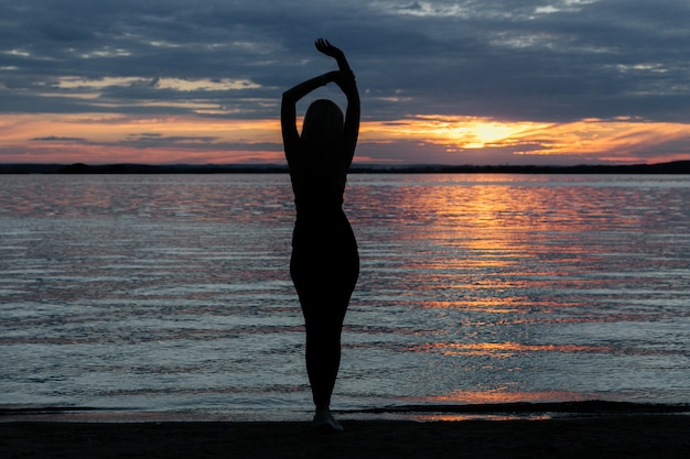 Silueta de una niña con una hermosa figura al atardecer junto al mar