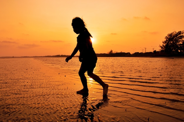 Silueta de niña jugando en la playa al atardecer