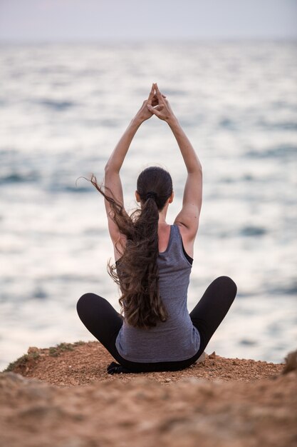 Silueta de una niña que hace yoga al atardecer cerca del mar