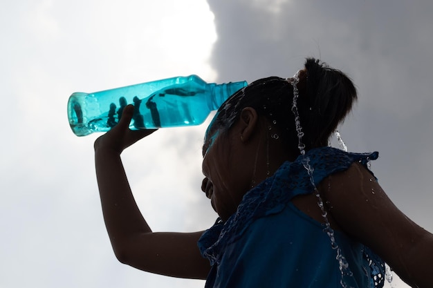 Foto silueta de una niña salpicando agua en la cabeza de una botella de plástico azul bajo el cielo para enfriarse