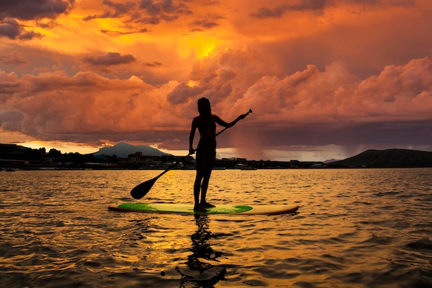 Silueta de una niña en Stand Up Paddle Board en el fondo del cielo tormentoso SUP