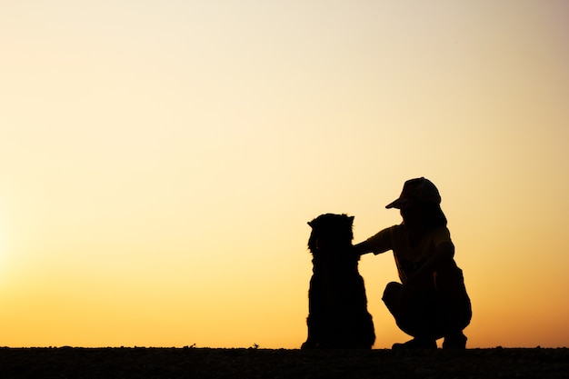 Silueta de niña y su perro con fondo hermoso atardecer.