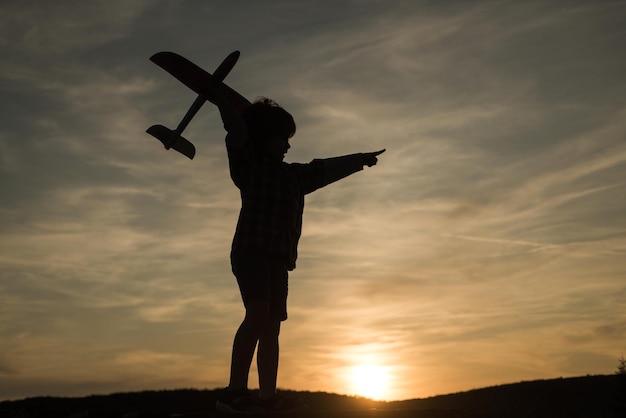 Silueta de niño con avión de juguete en rayos de sol Niño piloto aviador con avión sueña con t