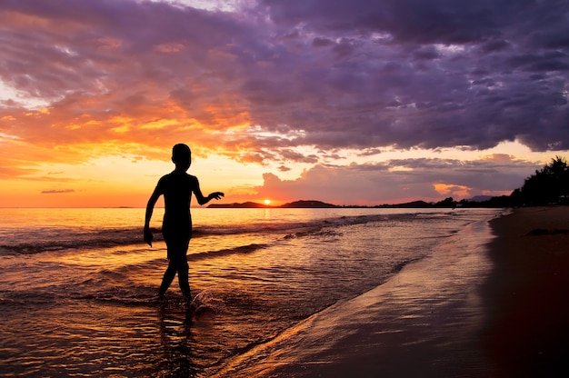 Silueta de niño caminando en la playa al atardecer