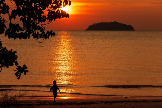 La silueta de un niño corriendo hacia la orilla del agua al atardecer Hermoso paisaje marino al atardecer