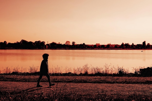 Silueta de niño un niño solitario caminando por el río al atardecer