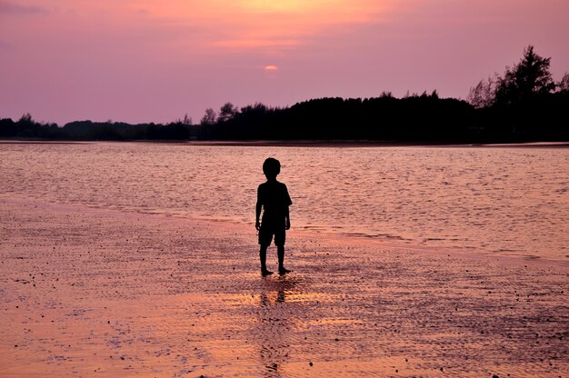 Silueta de niño solitario de pie en la playa al atardecer