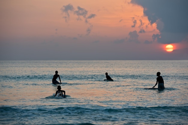 Silueta de niños navegando en tablas en la orilla del mar durante la puesta de sol