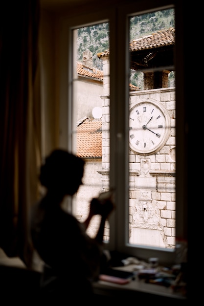 Silueta de la novia de pie junto a la ventana en una habitación de hotel antes de la ceremonia de la boda