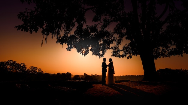 Silueta de novios enamorados besándose y tomados de la mano juntos durante la puesta de sol con el cielo de la tarde