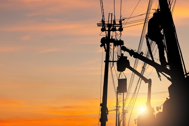 Foto silueta de un oficial electricista que sube a un poste utiliza un teleférico para mantener un sistema de líneas de alto voltaje