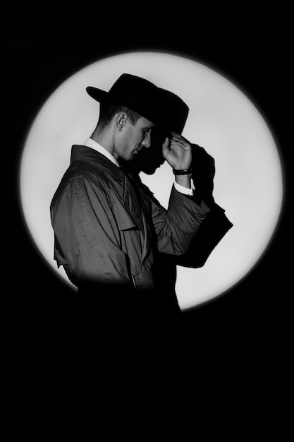 Foto una silueta oscura de un detective masculino con abrigo y sombrero al estilo noir un retrato dramático al estilo de las películas de detectives de la década de 1950 una silueta en un círculo de luz como el agente 007