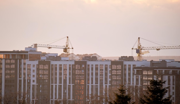 Silueta oscura de grúas torre en el sitio de construcción de edificios residenciales altos al atardecer Desarrollo inmobiliario