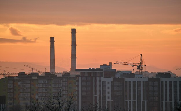 Silueta oscura de grúas torre en el sitio de construcción de edificios residenciales altos al atardecer Desarrollo inmobiliario