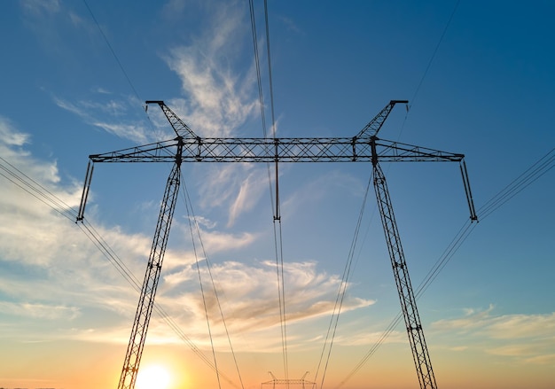 Silueta oscura de torre de alta tensión con líneas de energía eléctrica al amanecer Transmisión del concepto de energía eléctrica