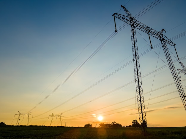 Silueta oscura de torres de alta tensión con líneas eléctricas al amanecer.