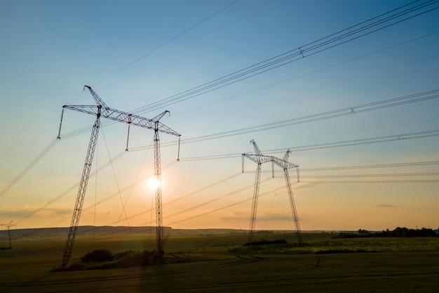 Silueta oscura de torres de alta tensión con líneas eléctricas al amanecer.