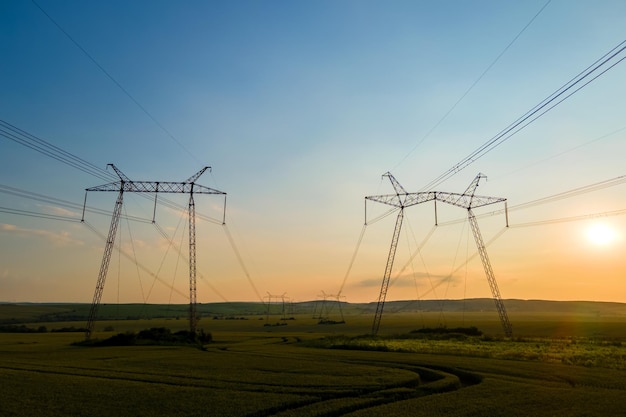 Silueta oscura de torres de alta tensión con líneas eléctricas al amanecer.