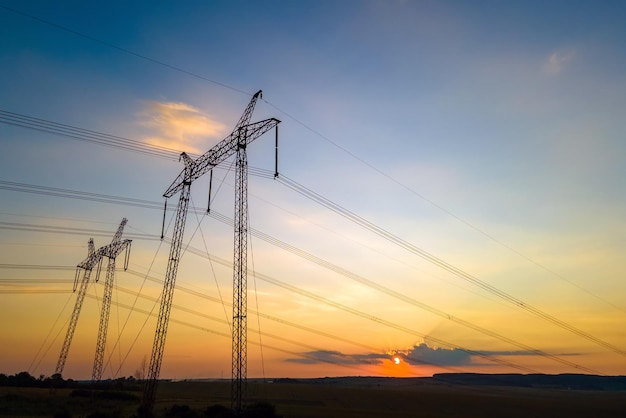 Silueta oscura de torres de alta tensión con líneas eléctricas al amanecer.