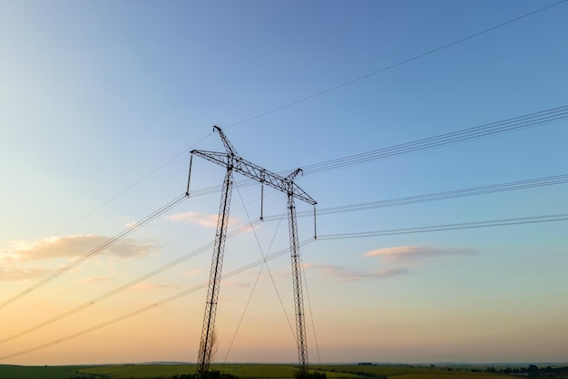 Silueta oscura de torres de alta tensión con líneas eléctricas al amanecer.