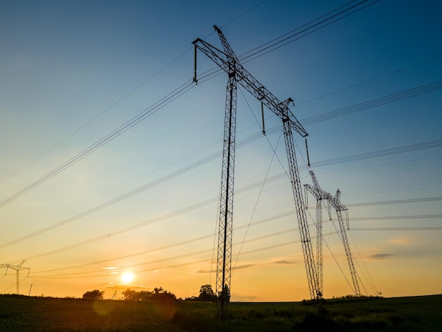 Silueta oscura de torres de alta tensión con líneas eléctricas al amanecer.