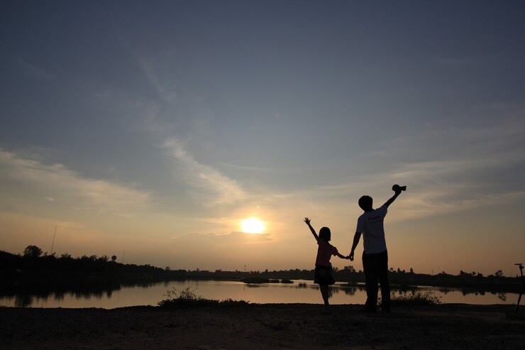 La silueta de padre e hijo estaba de pie cogidos de la mano brazos lago al atardecer.