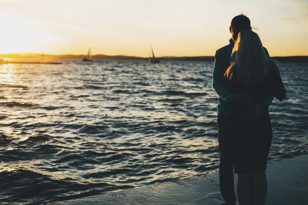 Silueta de pareja enamorada en el muelle, atardecer, veleros