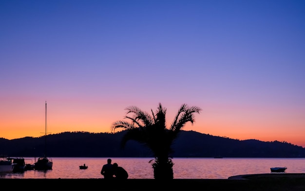 Silueta de una pareja joven admirando la puesta de sol contra el fondo del mar una cita para los amantes Fondo de vacaciones o idea de papel tapiz