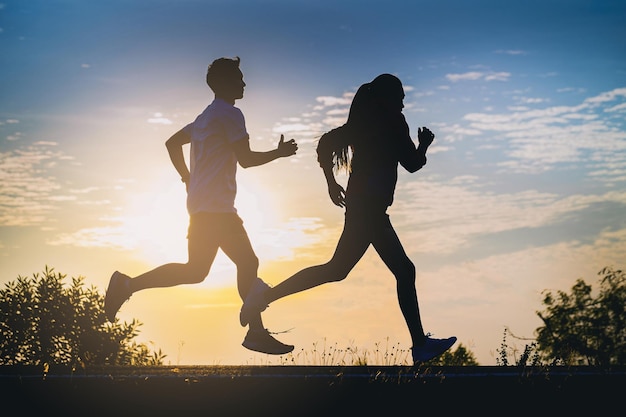 silueta, de, pareja joven, correr juntos, en, roadtrack