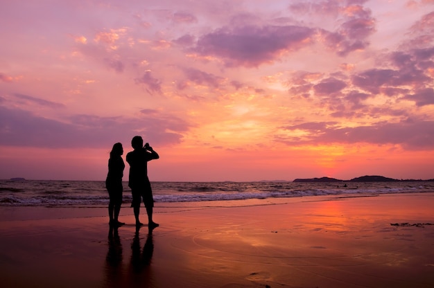 Silueta de pareja romántica de pie en la playa al atardecer