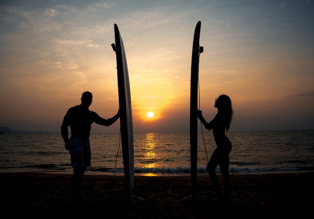 Silueta de pareja de surfistas con largas tablas de surf al atardecer