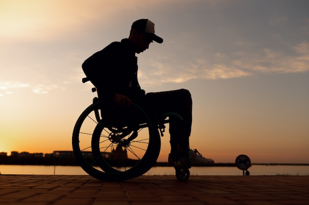 Silueta de una persona discapacitada en silla de ruedas en el fondo de la foto de alta calidad del atardecer