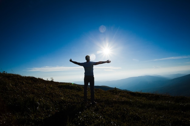 Silueta de una persona con las manos levantadas durante la puesta de sol en la cima de la montaña