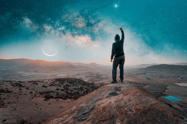 Silueta de persona parada en la cima de la montaña mirando la Vía Láctea y la Luna