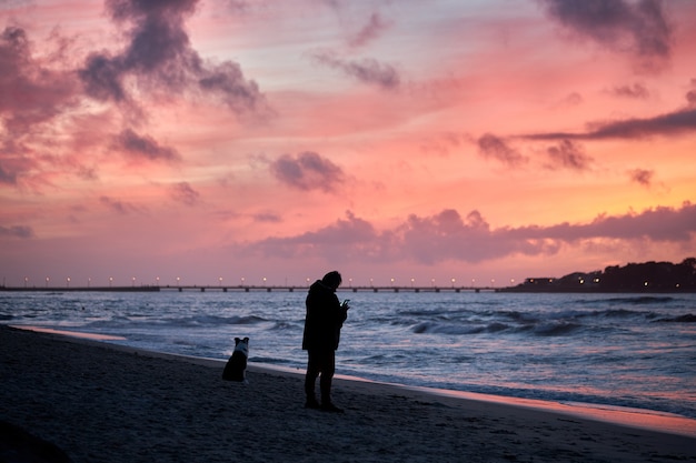 Silueta de una persona paseando a su perro en una playa un día con una puesta de sol roja