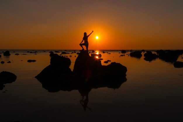 Foto silueta de una persona en una roca en la playa durante la puesta de sol