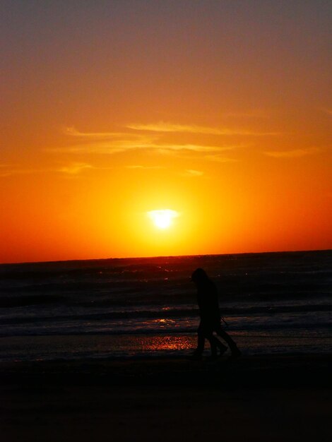 Foto silueta de personas caminando por la playa durante la puesta de sol