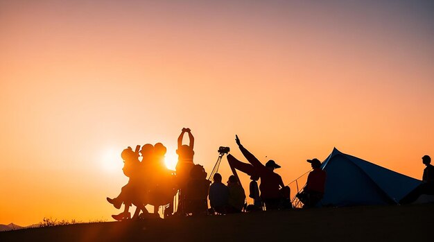 Una silueta de personas del grupo se divierten en la cima de la montaña cerca de la carpa durante la puesta de sol